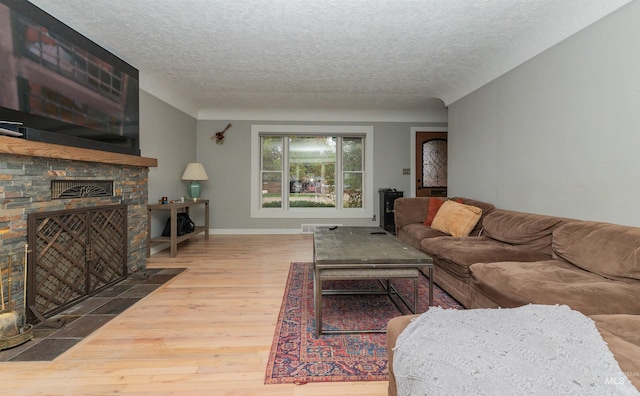 living room featuring baseboards, a large fireplace, a textured ceiling, and wood finished floors