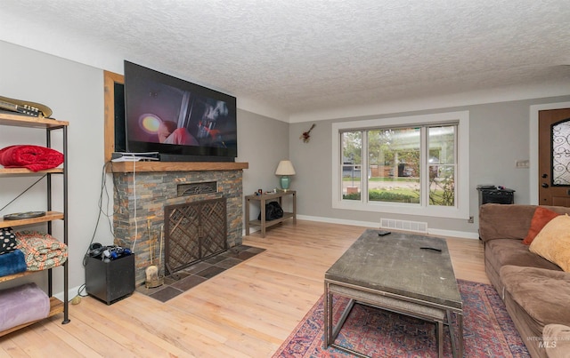 living room with baseboards, a stone fireplace, a textured ceiling, visible vents, and wood finished floors