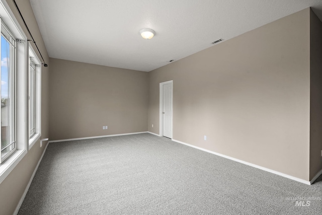 carpeted empty room featuring baseboards, visible vents, and plenty of natural light