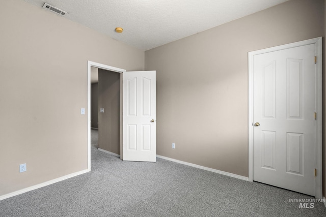 unfurnished bedroom featuring carpet floors, a textured ceiling, baseboards, and visible vents