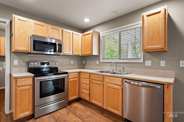 kitchen featuring light brown cabinetry, wood finished floors, light countertops, a sink, and stainless steel appliances