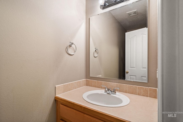 bathroom with vanity, a textured wall, and visible vents