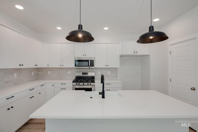 kitchen with white cabinets, light hardwood / wood-style flooring, an island with sink, appliances with stainless steel finishes, and decorative light fixtures