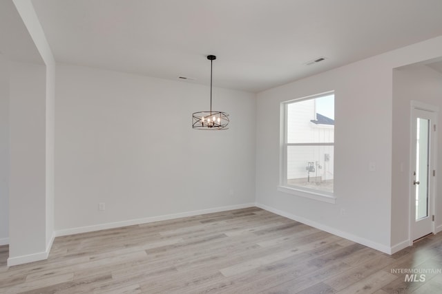 spare room with a notable chandelier and light wood-type flooring