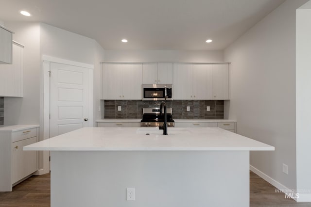 kitchen featuring white cabinetry, decorative backsplash, stainless steel appliances, and a center island with sink