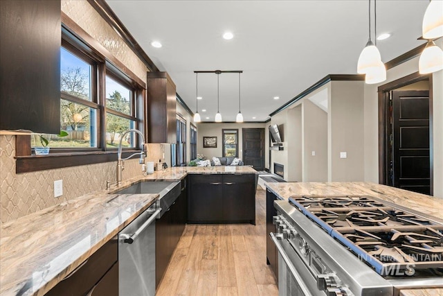 kitchen with pendant lighting, sink, light wood-type flooring, light stone countertops, and stainless steel appliances