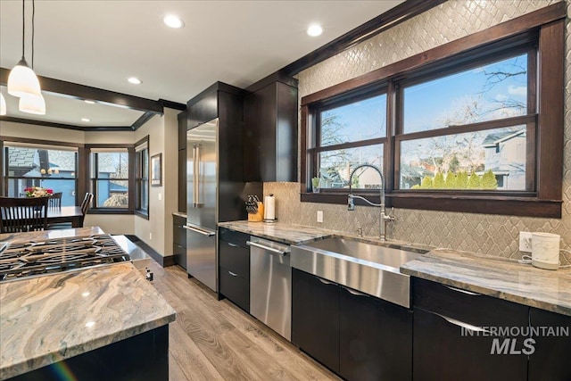 kitchen with light stone counters, sink, pendant lighting, and stainless steel appliances