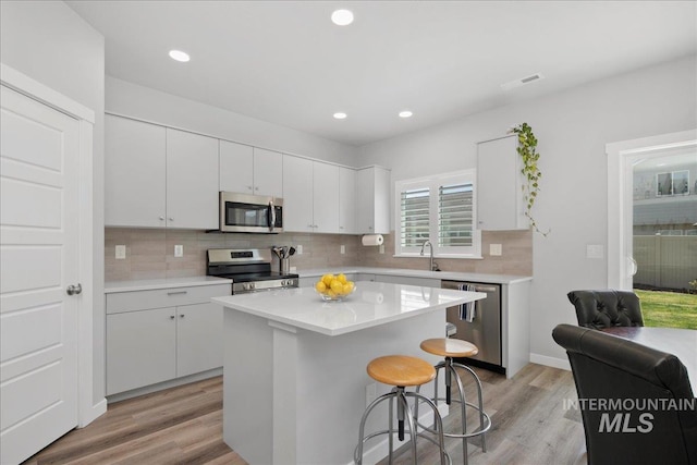 4953 W Apgar St, Meridian, ID 83646 - kitchen with stainless steel appliances, light wood-style flooring, white cabinets, tasteful backsplash, and a kitchen breakfast bar