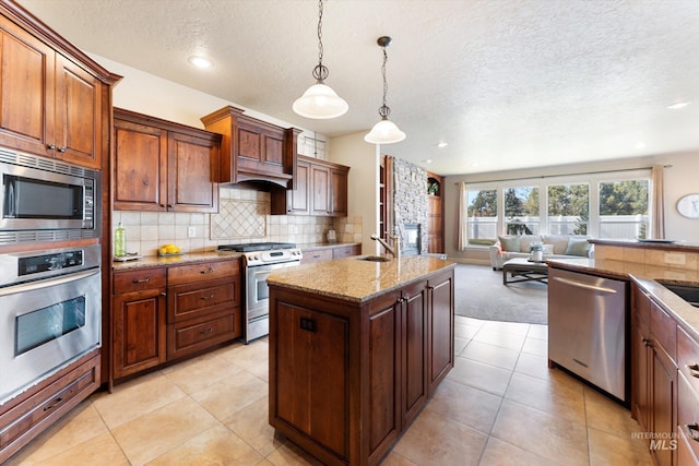 kitchen featuring open floor plan, decorative light fixtures, light stone countertops, a kitchen island with sink, and stainless steel appliances