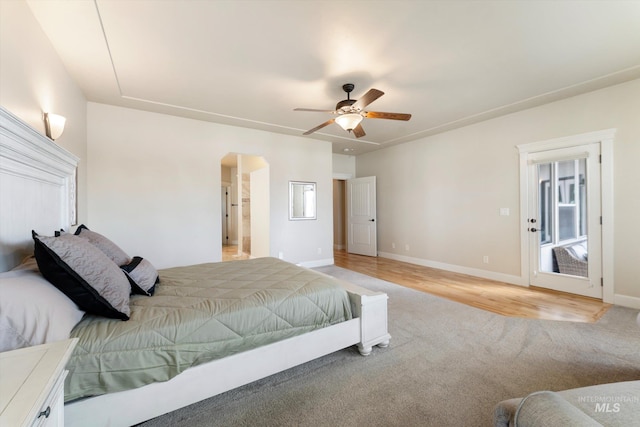 bedroom with a ceiling fan, arched walkways, light wood finished floors, and baseboards