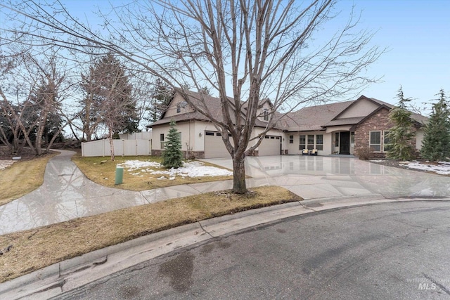 view of front facade with stucco siding, an attached garage, fence, stone siding, and driveway