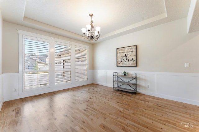 empty room featuring a raised ceiling, wainscoting, a notable chandelier, and wood finished floors