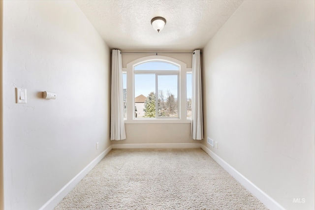 empty room featuring a textured ceiling, carpet flooring, visible vents, and baseboards