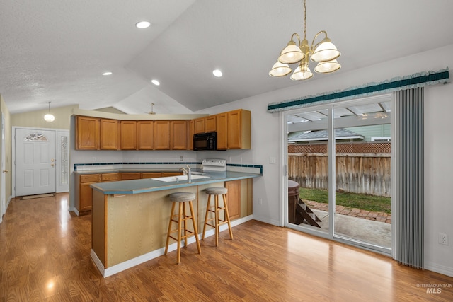 kitchen with black microwave, lofted ceiling, a peninsula, stove, and brown cabinetry