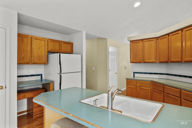 kitchen featuring baseboards, brown cabinets, wood finished floors, freestanding refrigerator, and a sink