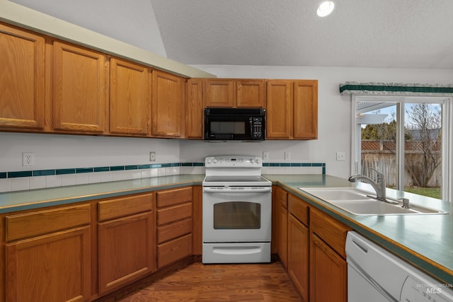 kitchen featuring a textured ceiling, white appliances, brown cabinetry, and a sink