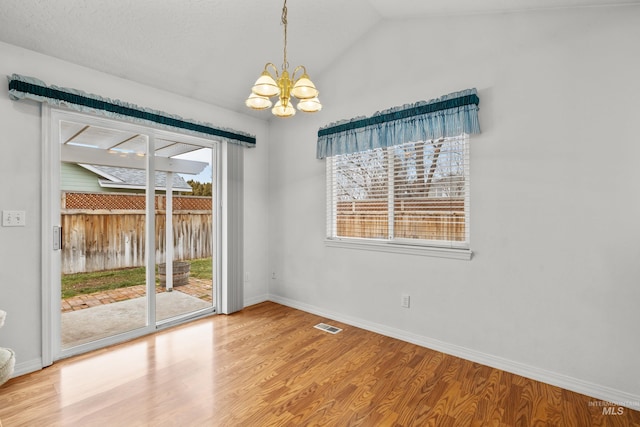 spare room featuring lofted ceiling, visible vents, wood finished floors, a chandelier, and baseboards