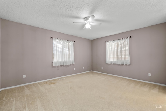 carpeted empty room featuring visible vents, a textured ceiling, baseboards, and a ceiling fan