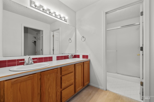 bathroom with a stall shower, double vanity, a sink, and tile patterned floors