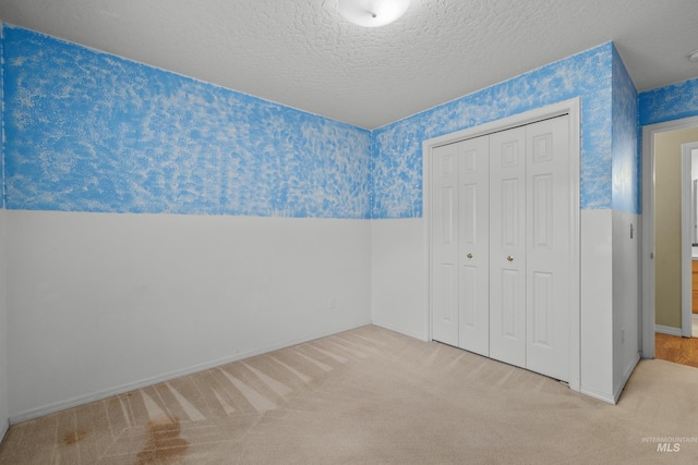 unfurnished bedroom featuring a textured ceiling, a closet, and light carpet