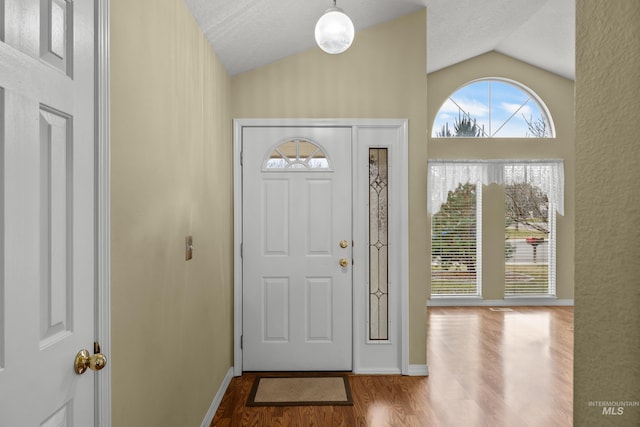 entryway featuring vaulted ceiling, a textured ceiling, baseboards, and wood finished floors