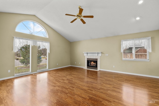 unfurnished living room featuring baseboards, ceiling fan, a tiled fireplace, and wood finished floors