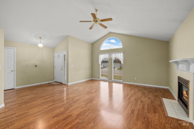 unfurnished living room with light wood finished floors, baseboards, vaulted ceiling, and a tiled fireplace