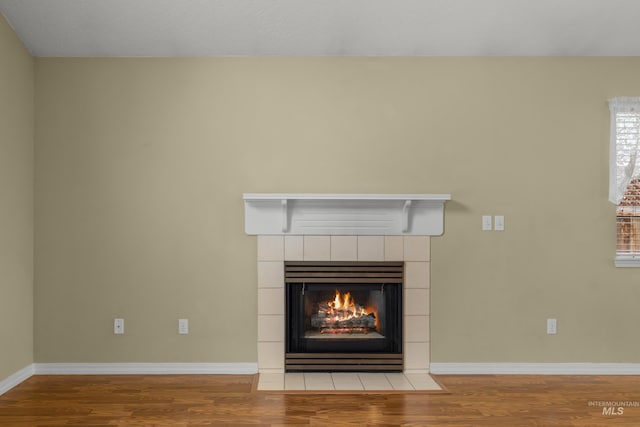 room details with a tiled fireplace, baseboards, and wood finished floors