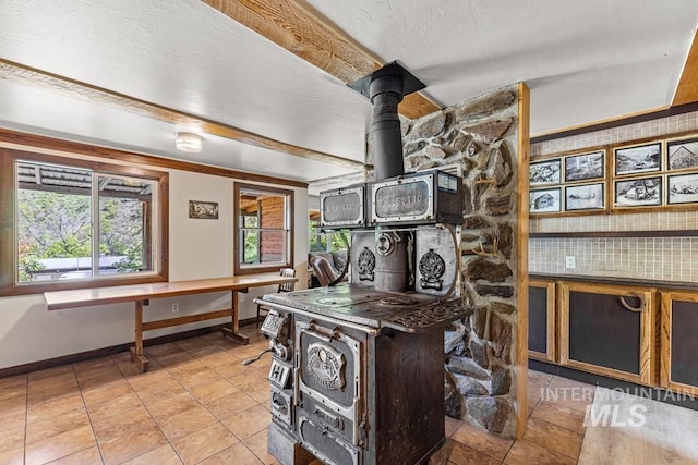 255 Seven U Ranch Rd, Lucile, ID 83542 - kitchen featuring baseboards, light tile patterned flooring, a wood stove, and beam ceiling
