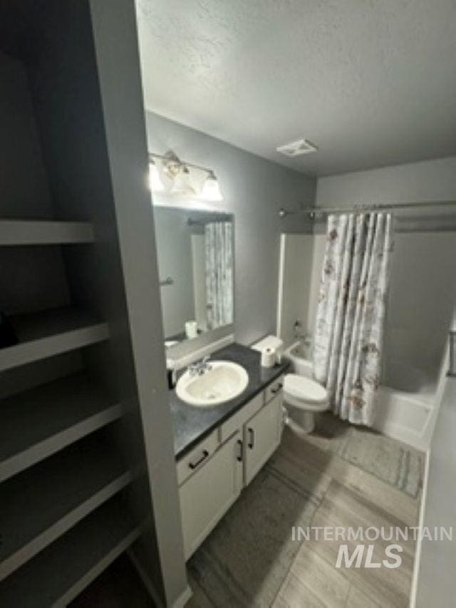 bathroom featuring visible vents, toilet, a textured ceiling, shower / tub combo, and vanity