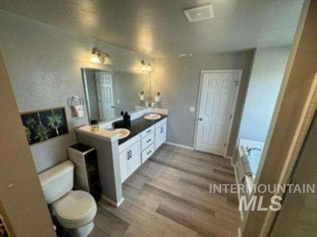 full bath featuring wood finished floors, double vanity, a sink, a garden tub, and toilet