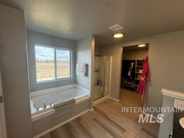 bathroom with wood finished floors, a shower stall, a spacious closet, a bath, and vanity