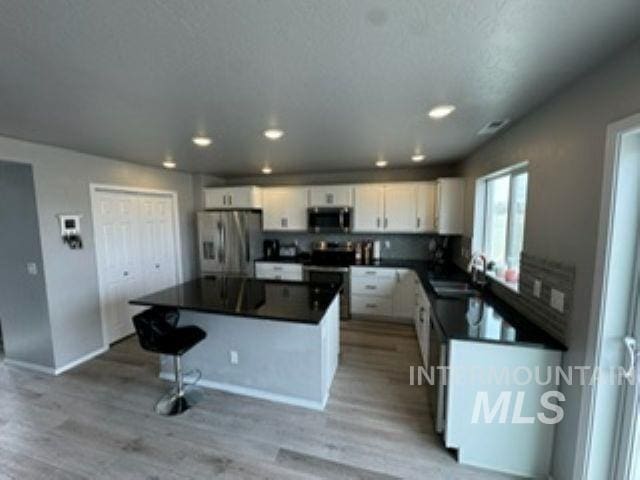 kitchen with a sink, dark countertops, a center island, white cabinetry, and stainless steel appliances