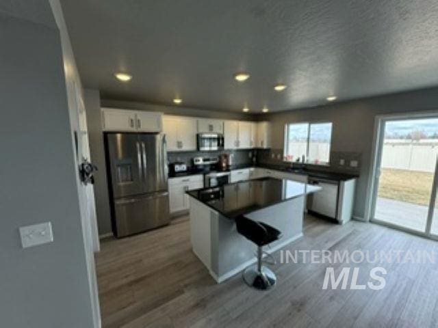 kitchen with dark countertops, a center island, white cabinetry, appliances with stainless steel finishes, and light wood finished floors