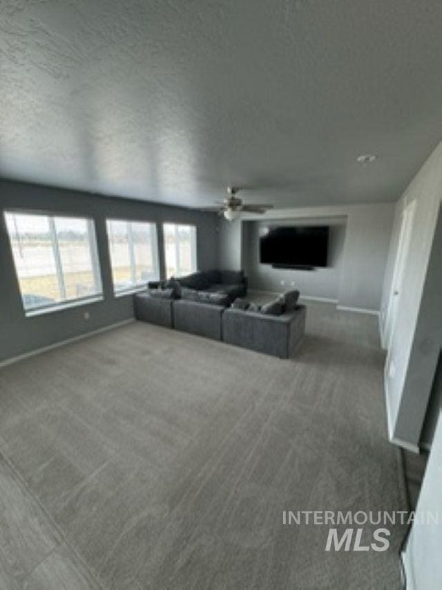 unfurnished living room featuring a ceiling fan, baseboards, carpet floors, and a textured ceiling