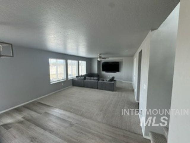 unfurnished living room with baseboards, wood finished floors, a textured ceiling, and ceiling fan