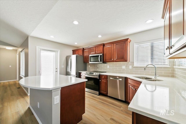 kitchen featuring sink, backsplash, a center island, stainless steel appliances, and light wood-type flooring