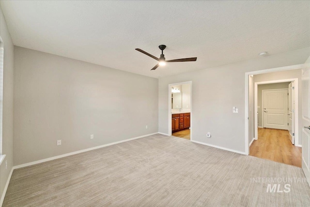 unfurnished bedroom with ceiling fan, light colored carpet, connected bathroom, and a textured ceiling