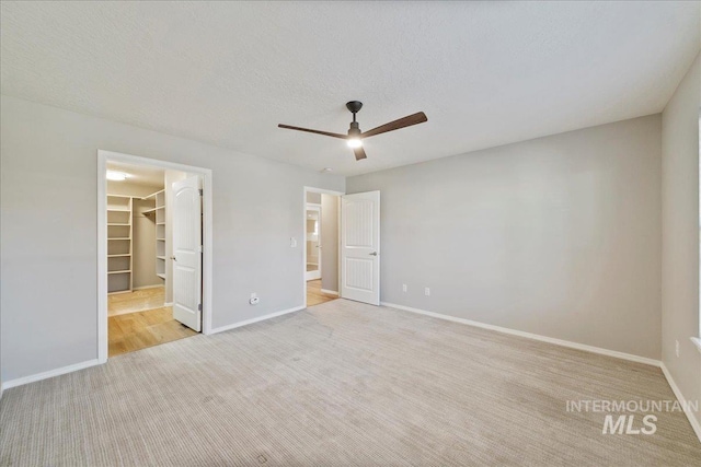 unfurnished bedroom featuring ceiling fan, a textured ceiling, light carpet, a spacious closet, and a closet