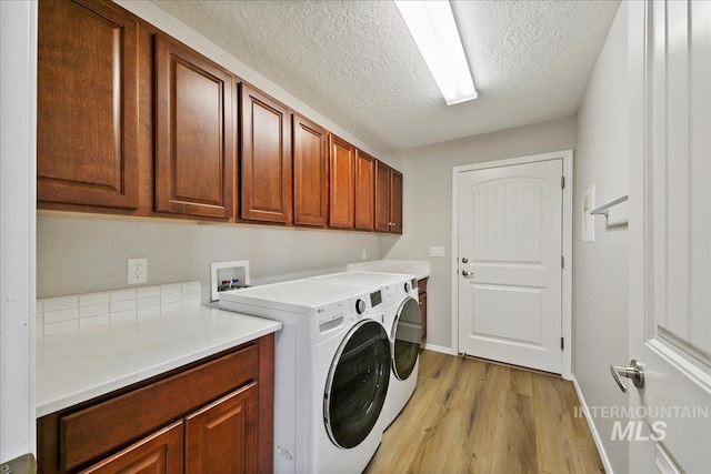 laundry area with cabinets, a textured ceiling, washing machine and clothes dryer, and light hardwood / wood-style floors