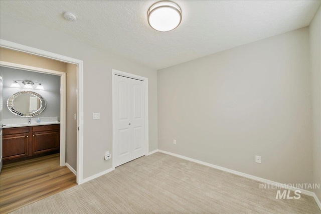 unfurnished bedroom featuring a closet, sink, light carpet, and a textured ceiling