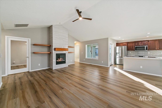 unfurnished living room with high vaulted ceiling, a large fireplace, hardwood / wood-style flooring, ceiling fan, and a textured ceiling