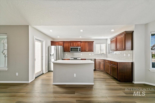 kitchen with tasteful backsplash, stainless steel appliances, wood-type flooring, and a kitchen island