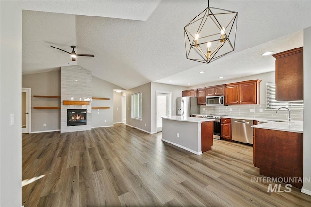 kitchen featuring a kitchen island, appliances with stainless steel finishes, decorative light fixtures, sink, and light wood-type flooring