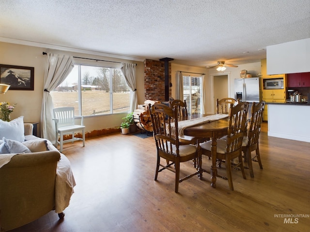 dining area featuring ceiling fan, hardwood / wood-style flooring, a textured ceiling, and a wood stove