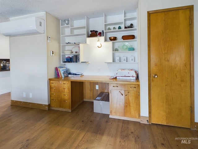 kitchen with an AC wall unit, dark hardwood / wood-style floors, built in desk, and a textured ceiling