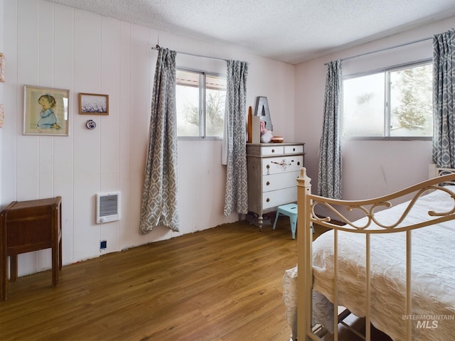 bedroom featuring wood-type flooring, heating unit, and a textured ceiling