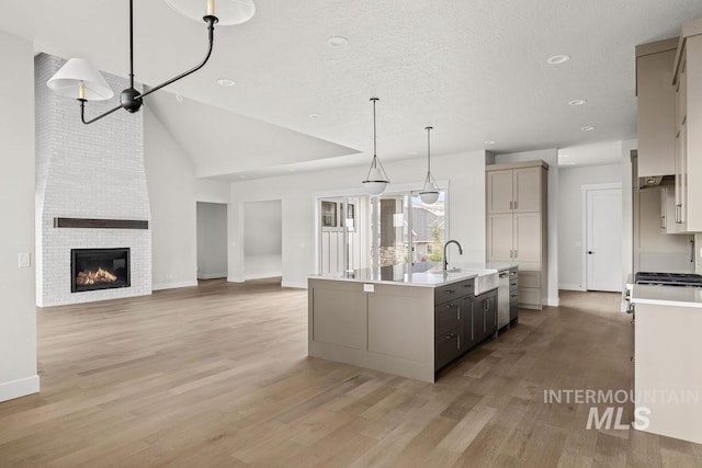 kitchen with sink, hanging light fixtures, a brick fireplace, an island with sink, and light hardwood / wood-style floors