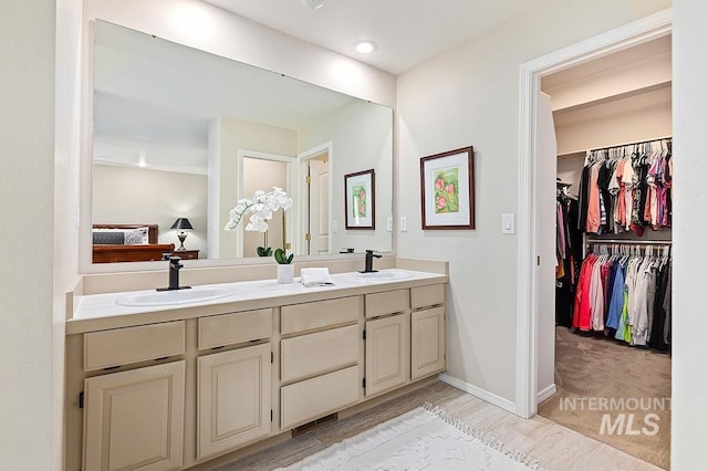 full bathroom featuring double vanity, connected bathroom, baseboards, and a sink