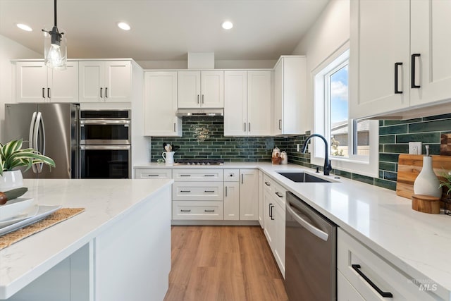 kitchen with stainless steel appliances, hanging light fixtures, white cabinetry, a sink, and under cabinet range hood